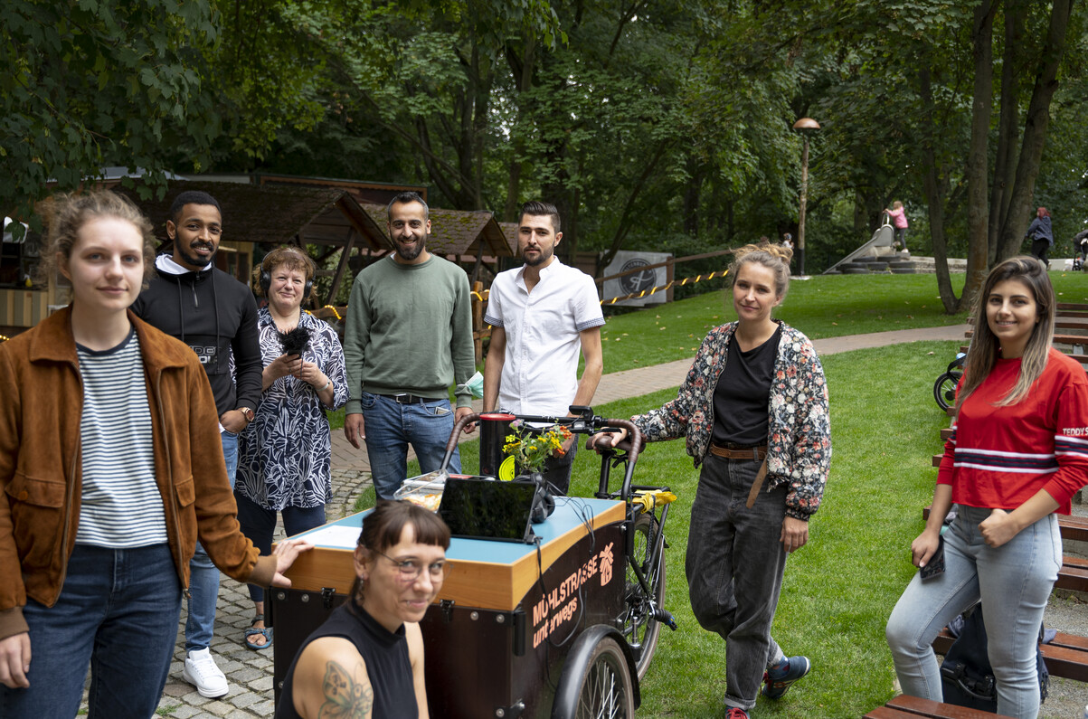 Verschiedene Menschen stehen um Stand herum, ein Mikrofon ist zu sehen.